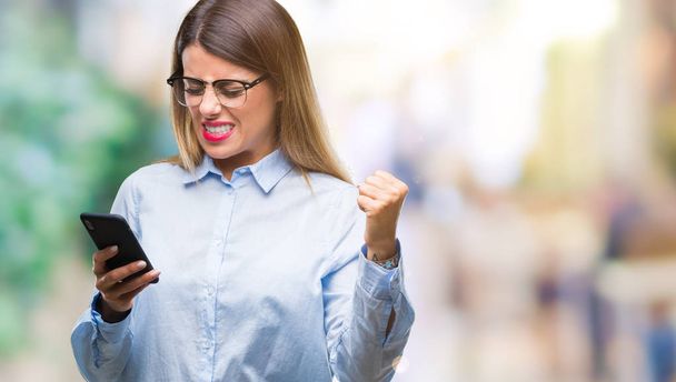 Jonge mooie zakelijke vrouw SMS bericht met behulp van smartphone over geïsoleerde achtergrond boos en gefrustreerd schreeuwen met woede, gek en schreeuwen met opgeheven hand, woede concept - Foto, afbeelding