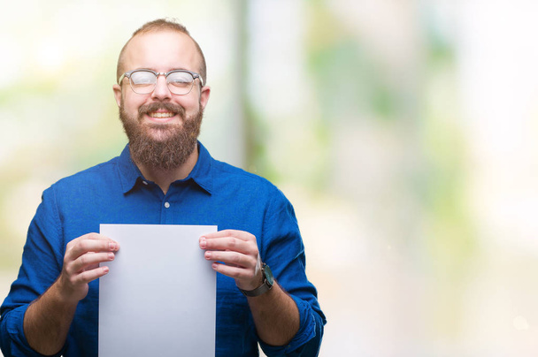Young hipster man wearing glasses and holding blank paper over isolated background with a happy face standing and smiling with a confident smile showing teeth - Photo, Image
