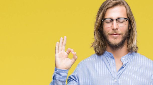 Young handsome man with long hair wearing glasses over isolated background relax and smiling with eyes closed doing meditation gesture with fingers. Yoga concept. - Photo, Image
