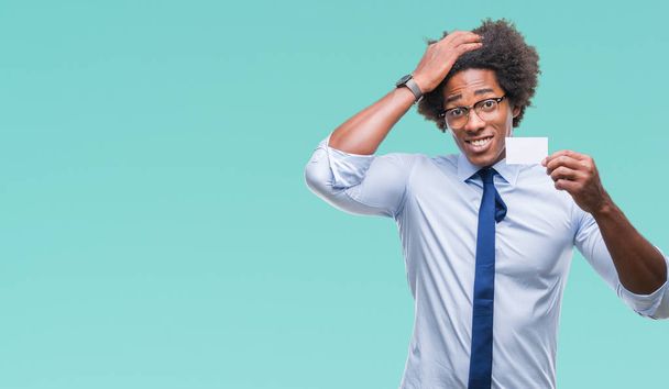 Afro Amerikaanse man houdt bezoek kaart over geïsoleerde achtergrond benadrukt met de hand op het hoofd, geschokt met schaamte en verrassing gezicht, boos en gefrustreerd. Angst en boos voor fout. - Foto, afbeelding