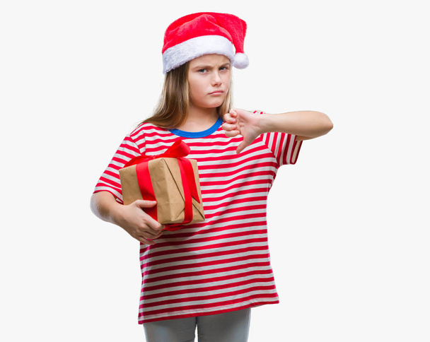 Mooi meisje dragen kerstmuts en bedrijf gift over geïsoleerde achtergrond met een boos gezicht, minteken weergegeven: afkeer met duimen naar beneden, afwijzing concept - Foto, afbeelding