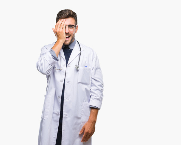 Young handsome doctor man over isolated background covering one eye with hand with confident smile on face and surprise emotion. - Фото, изображение