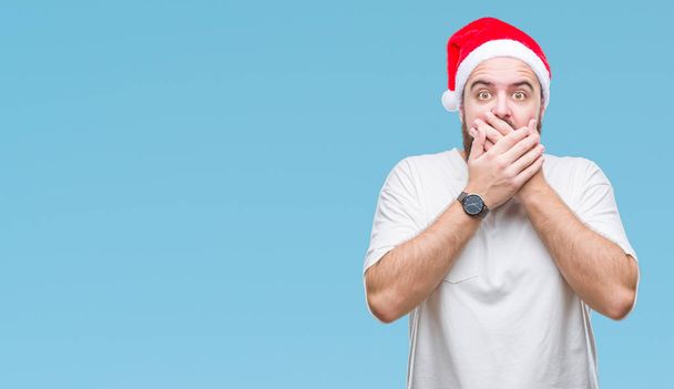 若い白人ヒップ男は孤立した背景のミスのための手で口を覆っているショックを受けた上クリスマス帽子をかぶっています。秘密の概念. - 写真・画像