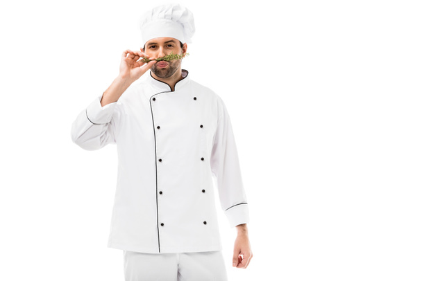 handsome young chef making mustache with thymes and looking at camera isolated on white - Photo, Image