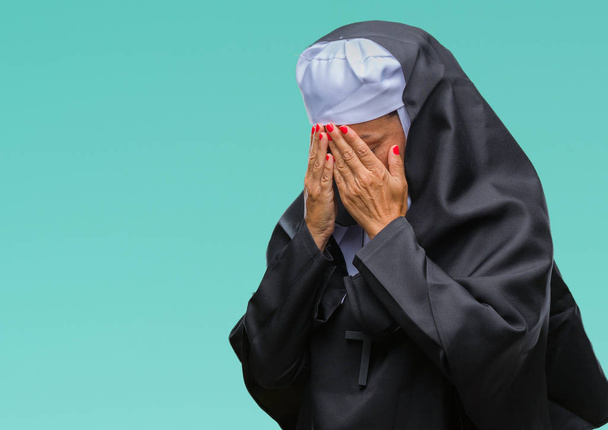 Μέσης ηλικίας γυναίκα ανώτερος χριστιανική καθολική μοναχή πέρα από το απομονωμένο υπόβαθρο με θλιβερή έκφραση που καλύπτουν το πρόσωπο με τα χέρια ενώ κλαίει. Έννοια της κατάθλιψης. - Φωτογραφία, εικόνα