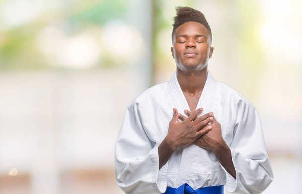 Young african american man over isolated background wearing kimono smiling with hands on chest with closed eyes and grateful gesture on face. Health concept. - Foto, imagen