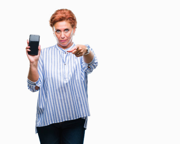Femme rousse caucasienne sénile attirante montrant l'écran du smartphone sur un arrière-plan isolé pointant du doigt la caméra et vers vous, signe de la main, geste positif et confiant de l'avant
 - Photo, image