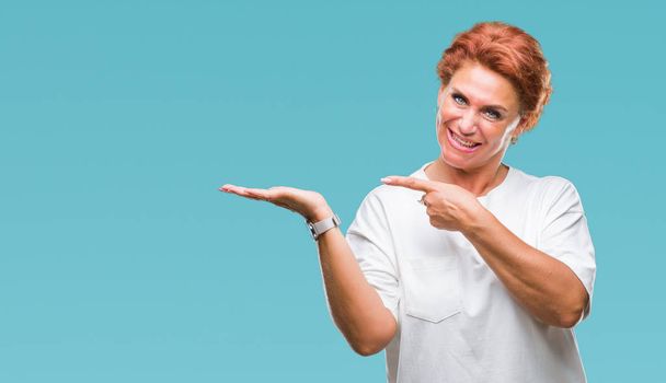 Atrractive senior caucasian redhead woman over isolated background amazed and smiling to the camera while presenting with hand and pointing with finger. - Fotó, kép