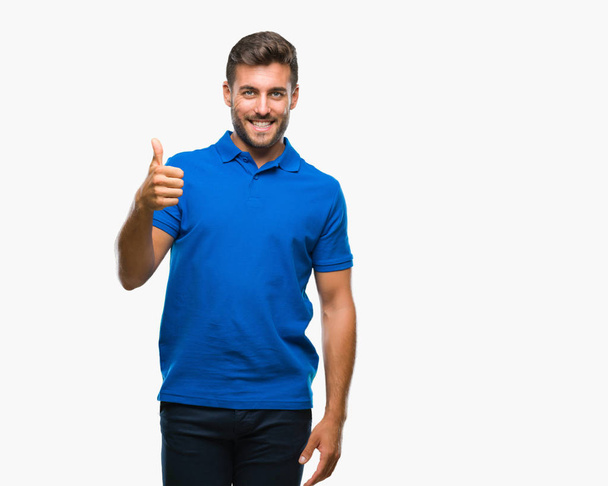 Young handsome man over isolated background doing happy thumbs up gesture with hand. Approving expression looking at the camera with showing success. - Photo, Image