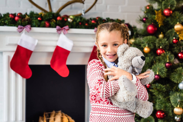adorable enfant heureux étreignant ours en peluche et souriant à la caméra au moment de Noël
 - Photo, image