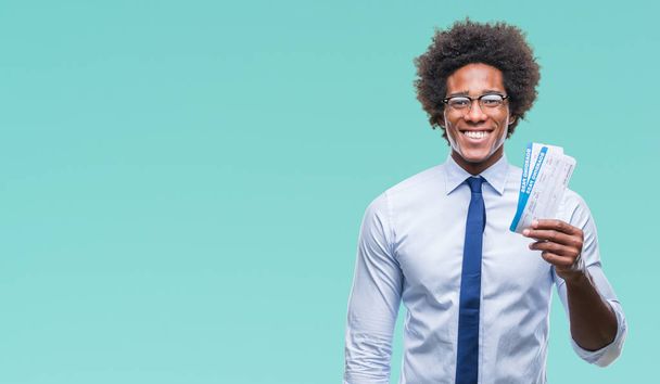 Афро-американец держит посадочный талон на изолированном фоне с счастливым лицом стоя и улыбаясь с уверенной улыбкой, показывая зубы
 - Фото, изображение