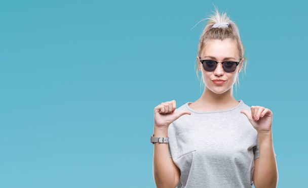 Young blonde woman wearing sunglasses over isolated background looking confident with smile on face, pointing oneself with fingers proud and happy. - Photo, Image