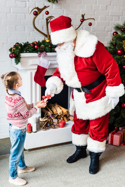 high angle view of little child giving rolled wishlist to santa - Photo, Image