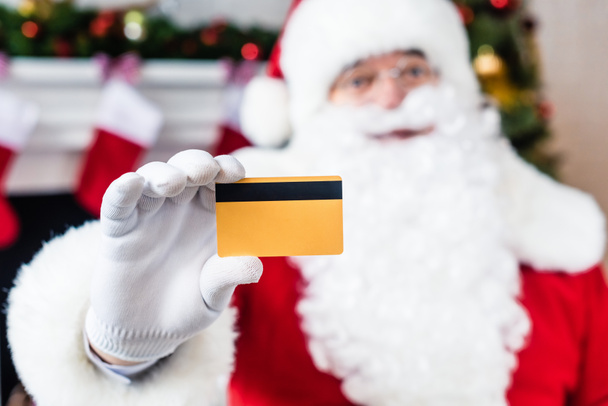 close-up view of santa claus holding credit card and looking at camera, selective focus - Foto, afbeelding