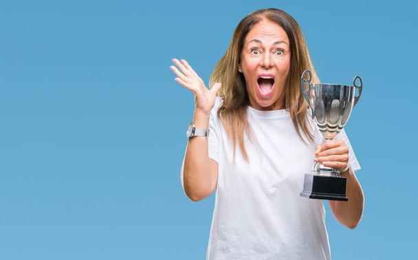 Orta yaş İspanyol kazanan kadın Ödülü holding trophy üzerinde kutluyor büyük gülümseme ile çığlık zaferini kutluyor ve ellerini kaldırdı arka plan çok mutlu ve heyecanlı, kazanan ifade izole - Fotoğraf, Görsel