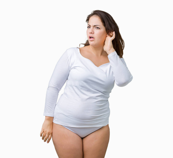 Beautiful plus size young overwight woman wearing white underwear over isolated background smiling with hand over ear listening an hearing to rumor or gossip. Deafness concept. - Photo, Image