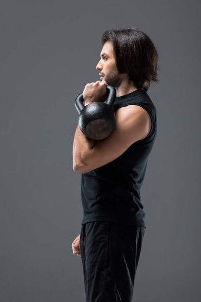 side view of muscular young man exercising with kettlebell isolated on grey - Foto, imagen