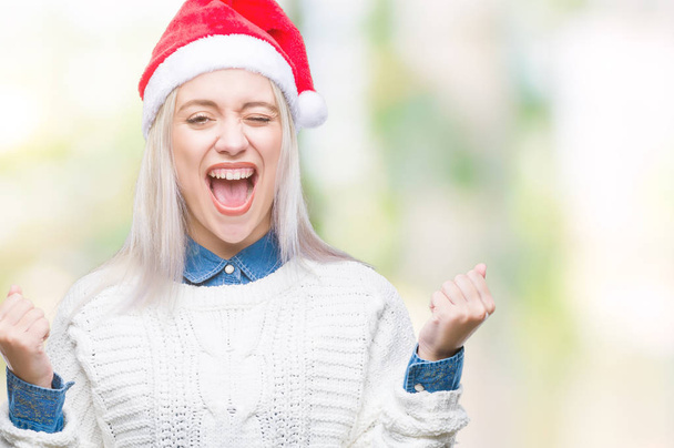 上孤立した背景を祝うクリスマス帽子をかぶっている若いブロンドの女性驚いて腕を上げると成功のため驚くし、目を開きます。勝者の概念. - 写真・画像