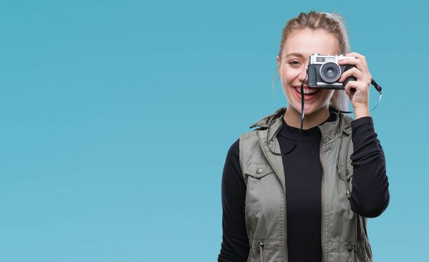 Молодая блондинка делает фотографии с помощью винтажной камеры на изолированном фоне с счастливым лицом стоя и улыбаясь с уверенной улыбкой показывая зубы
 - Фото, изображение