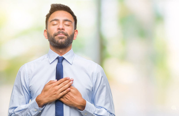 Adult hispanic business man over isolated background smiling with hands on chest with closed eyes and grateful gesture on face. Health concept. - Foto, Bild