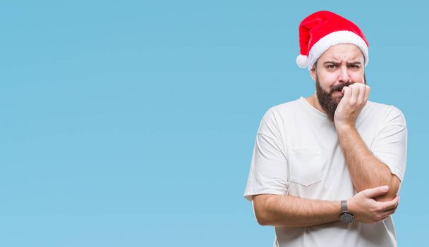 若い白人ヒップ男は不安や両手の爪を噛んで口の中で緊張を探して孤立の背景にクリスマス帽子をかぶっています。不安の問題. - 写真・画像