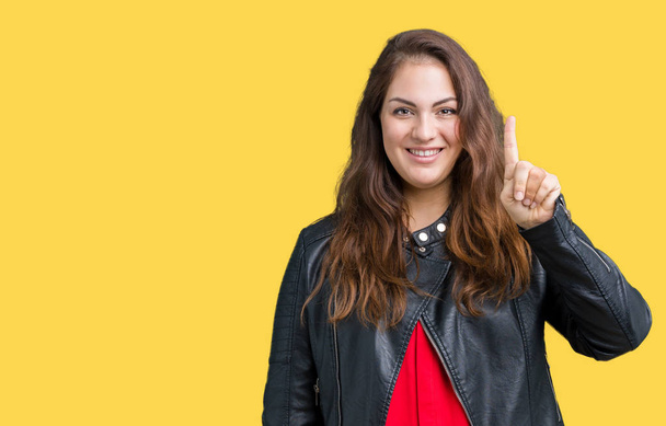Beautiful plus size young woman wearing a fashion leather jacket over isolated background showing and pointing up with finger number one while smiling confident and happy. - Φωτογραφία, εικόνα