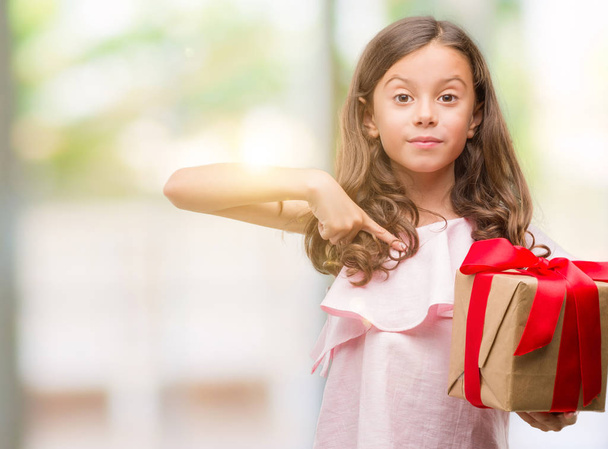 Morena chica hispana sosteniendo un regalo con la cara sorpresa señalando el dedo a sí mismo
 - Foto, Imagen