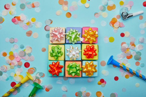 Top view of colorful gifts with bows, party horns and confetti on blue background - Fotó, kép
