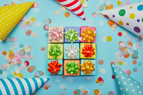 Bovenaanzicht van kleurrijke geschenken met bogen, feestmutsen en confetti op blauwe achtergrond - Foto, afbeelding