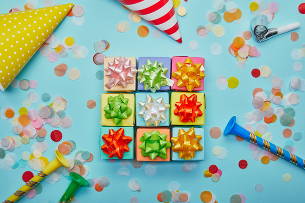 Vue du dessus de différents cadeaux colorés avec des arcs, des chapeaux de fête et des confettis sur fond bleu
 - Photo, image