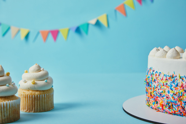 Sabrosos cupcakes y pastel sobre fondo azul con banderines
 - Foto, imagen