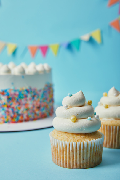 Delicious cupcake with sugar sprinkles on blue background with cake and bunting - Photo, Image