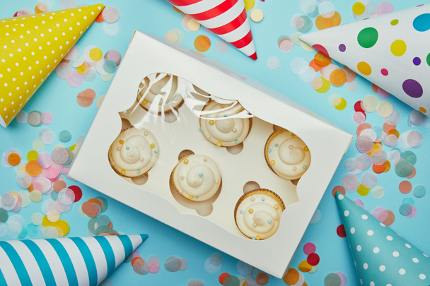 Top view of delicious cupcakes, party hats and confetti on blue background - Photo, Image