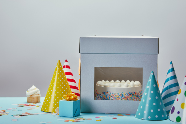 День рождения торт, шляпы, подарок и кекс на столе на сером фоне
 - Фото, изображение