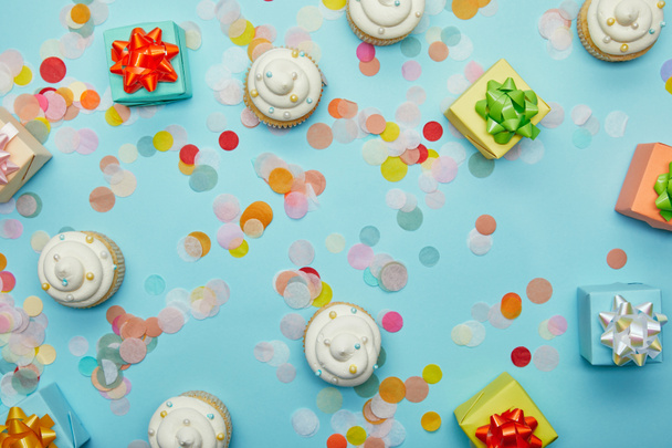 Vue du dessus de délicieux cupcakes, confettis et cadeaux sur fond bleu
 - Photo, image