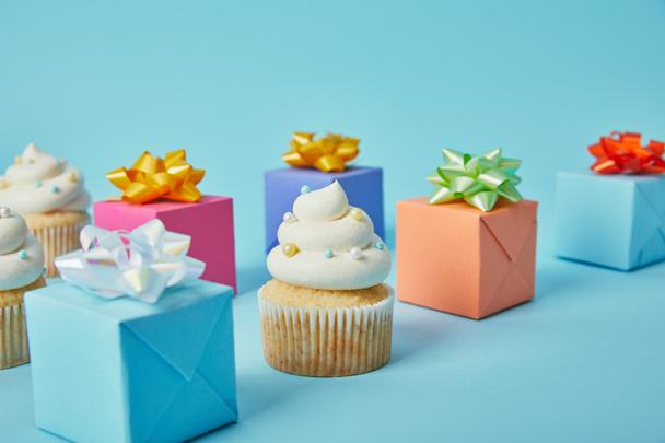 leckere Cupcakes und bunte Geschenke auf blauem Hintergrund - Foto, Bild