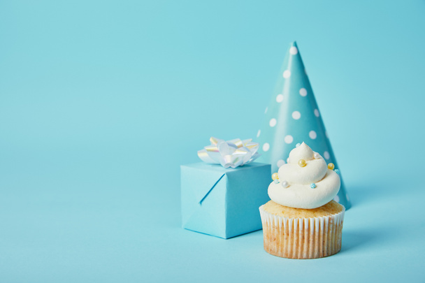 sombrero de fiesta, caja de regalo y delicioso cupcake sobre fondo azul
 - Foto, Imagen