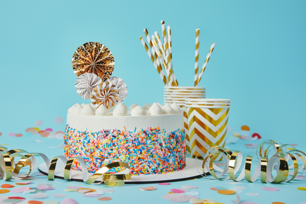 Delicious cake, plactic cups and drinking straws on blue background with confetti - Photo, Image