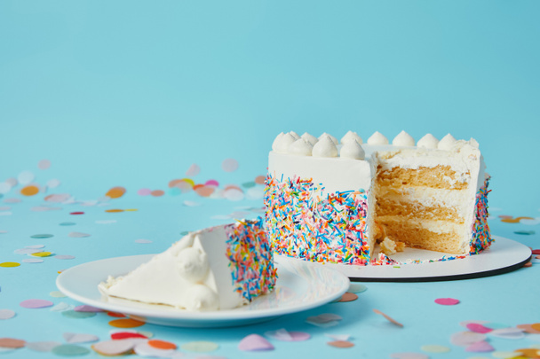 Slice of cake with cut cake on blue background with confetti - 写真・画像