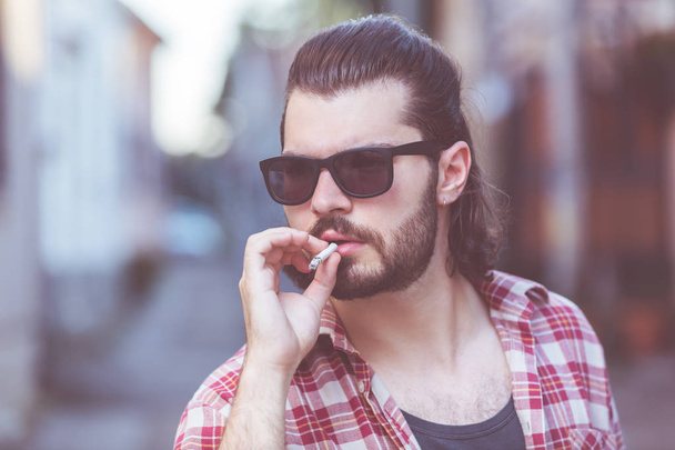 Jeune homme avec cigarette posant dans la rue
. - Photo, image