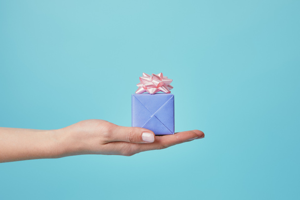 Partial view of woman holding gift with pink bow on blue background - Fotoğraf, Görsel
