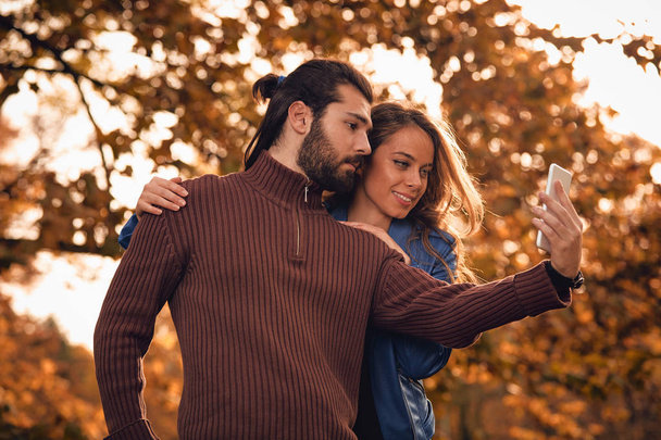 Молода пара використовує мобільний телефон в осінньому кольоровому парку
. - Фото, зображення