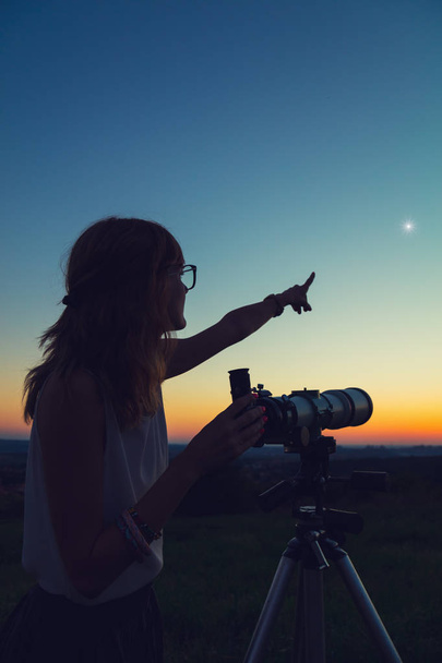 Nuori nainen pitelee tähtitieteellistä kaukoputkea ja katsoo taivasta
. - Valokuva, kuva