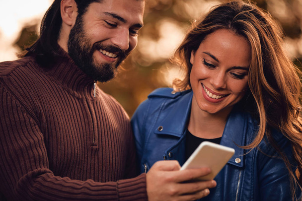 Jeune couple utilisant un téléphone portable en automne parc coloré
. - Photo, image