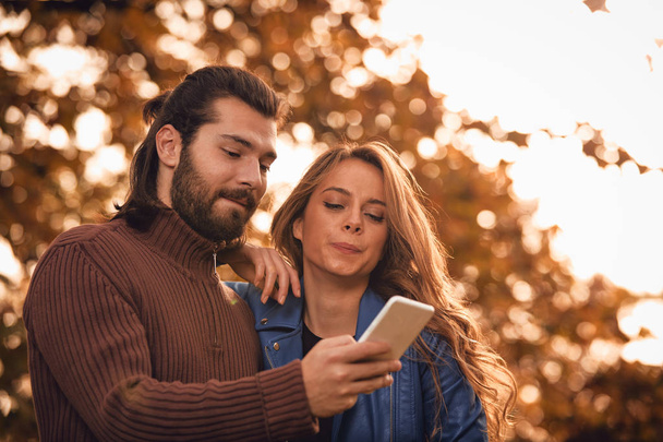 Młoda para przy użyciu telefonów komórkowych w jesień kolorowy park. - Zdjęcie, obraz