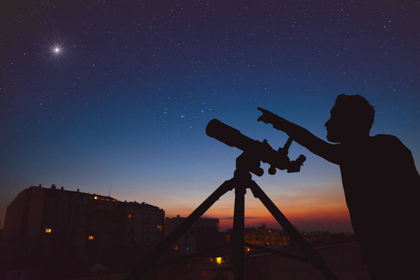 Молодий чоловік дивиться на небо з астрономічним телескопом в міському оточенні
. - Фото, зображення