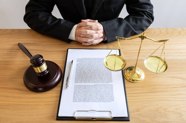 Legal law, advice and justice concept, male lawyer or notary working on a documents and report of the important case and wooden gavel, balance on table in courtroom. - Photo, Image