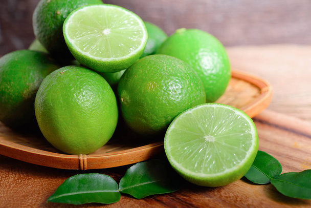 whole and half cut fresh lime in bamboo basket and on wooden background - Photo, Image