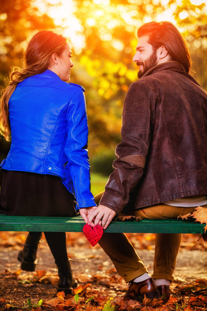 Couple holding heart-shape on a bench in the park. - Photo, Image