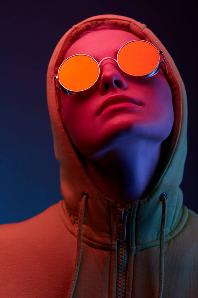 Neon portrait of young woman in round sunglasses and hoodie. Studio shot  - Foto, Imagen